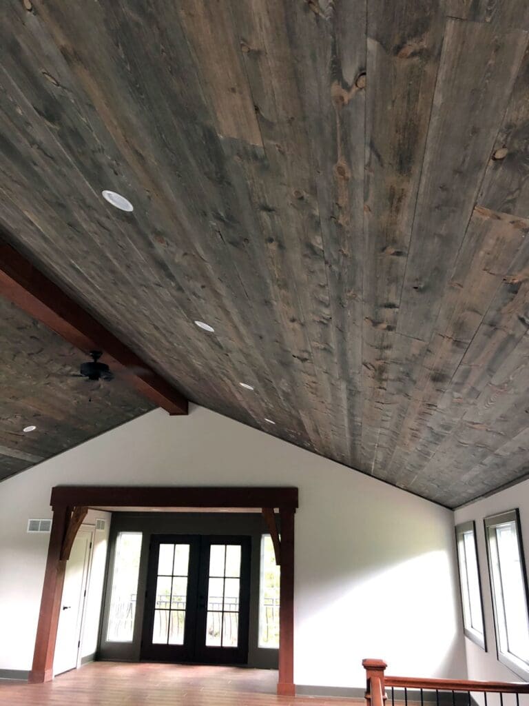 At the peak of a grey stained vaulted ceiling is a central, dark cherry stained beam.