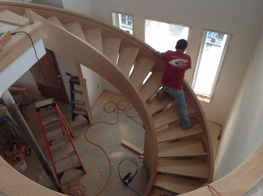 An incomplete, custom spiral staircase project with a worker halfway up the stairs