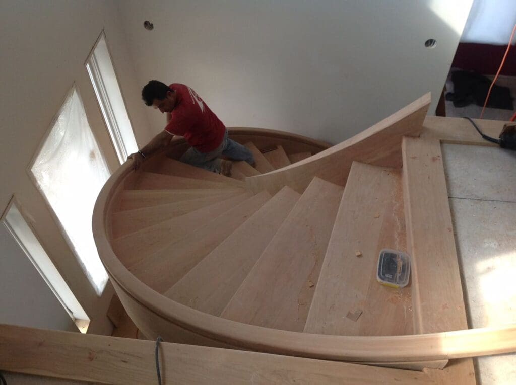 A second view of a worker partially up the stairs in an incomplete custom spiral staircase project