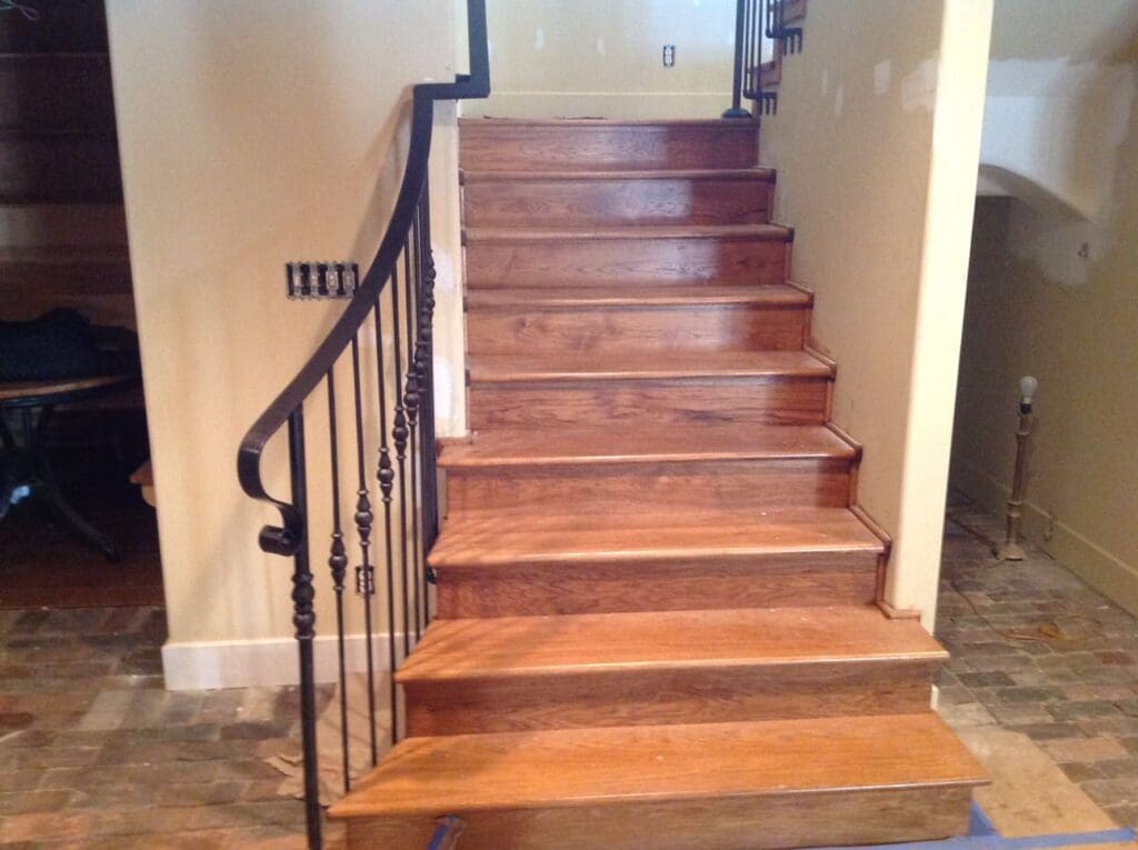 Wrought iron railing follows the length of a medium-stained, indoor wooden staircase