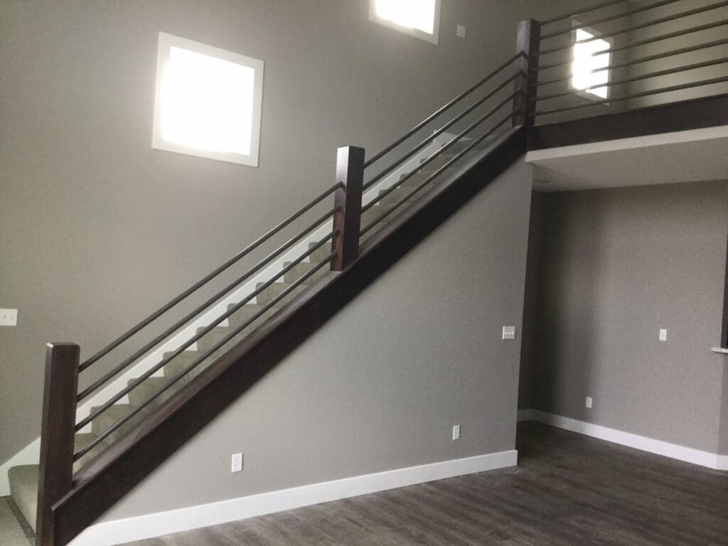 Dark finished wooden posts ajoin from metal piping to create a modern staircase that leads to a lofted second indoor floor