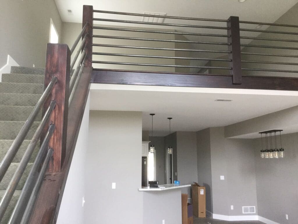 A lofted second floor is accessible from a modern staircase made from dark wooden posts and metal piping