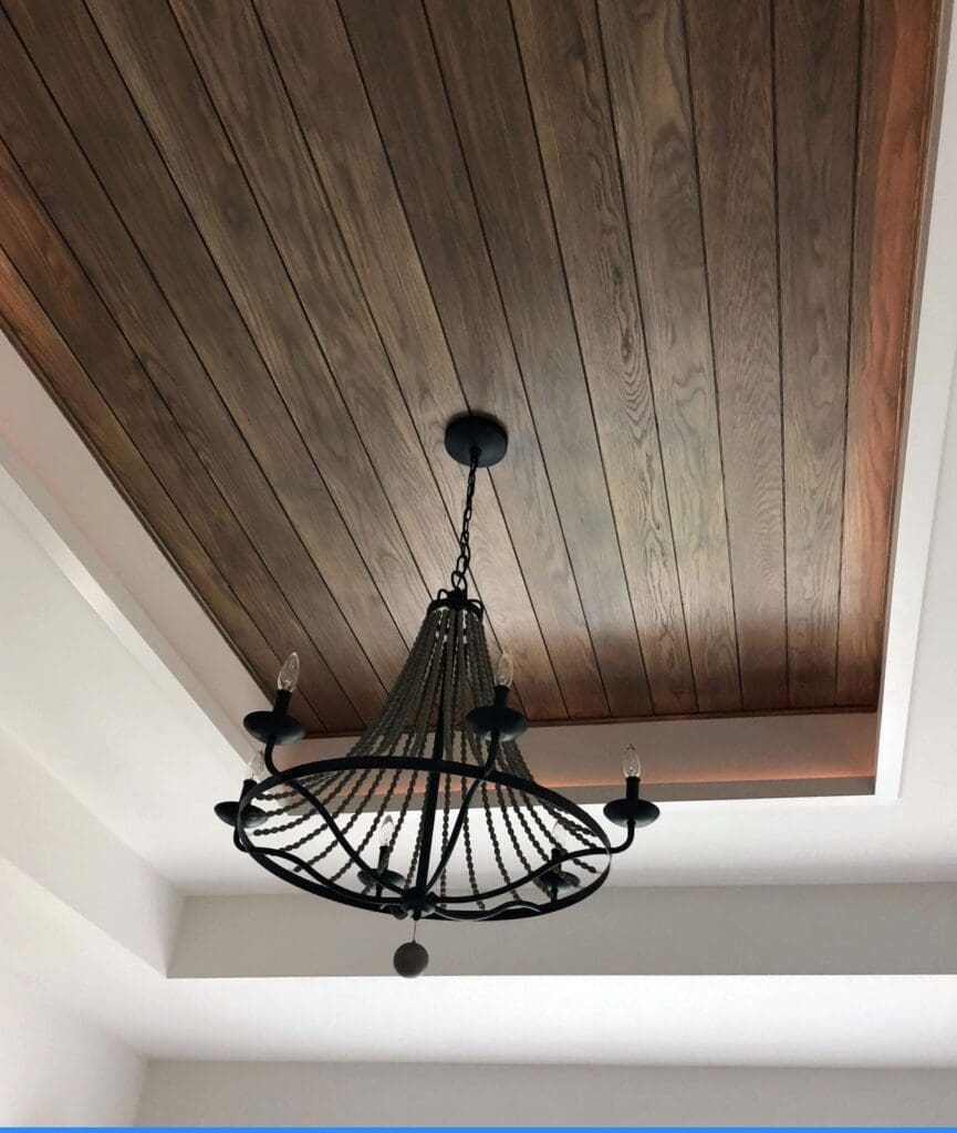 A narrow, recessed ceiling area is composed from beautifully stained wooden planks and a central chandelier