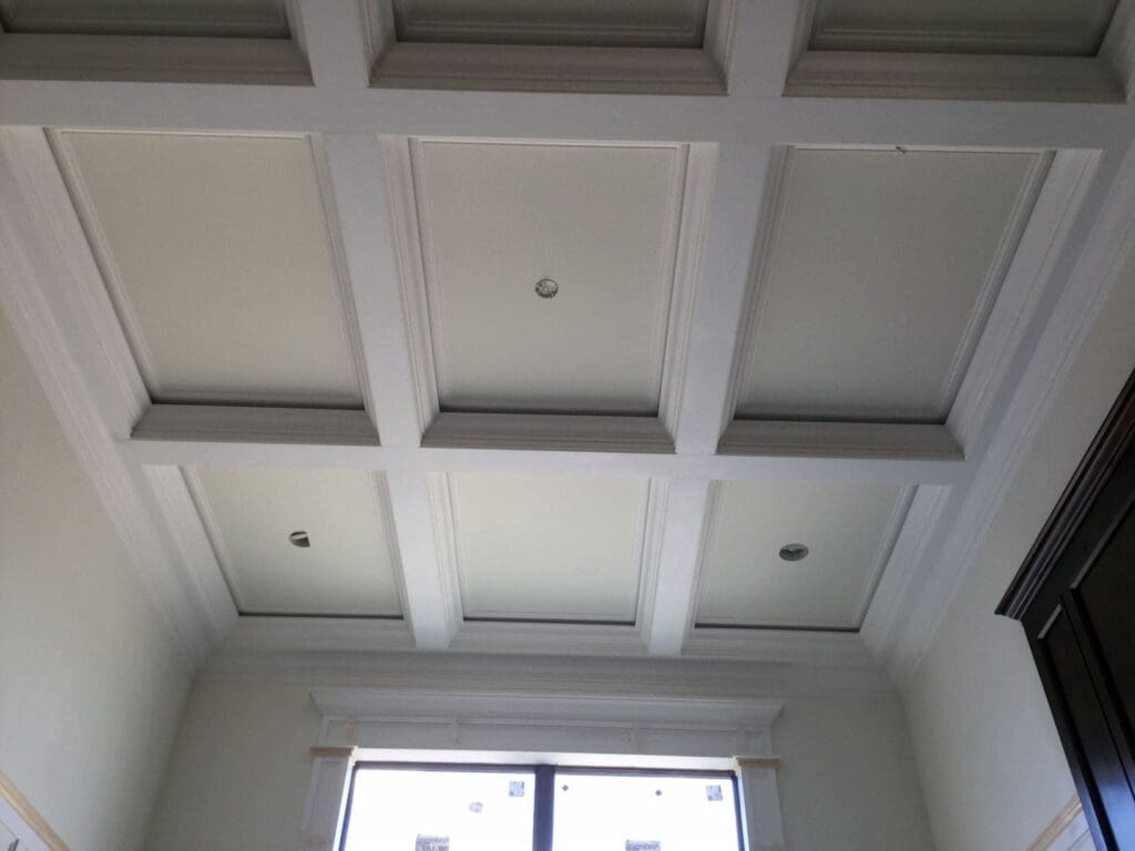 Neatly spaced beams line a ceiling in such a way that it's created outlines of 9 recessed rectangles