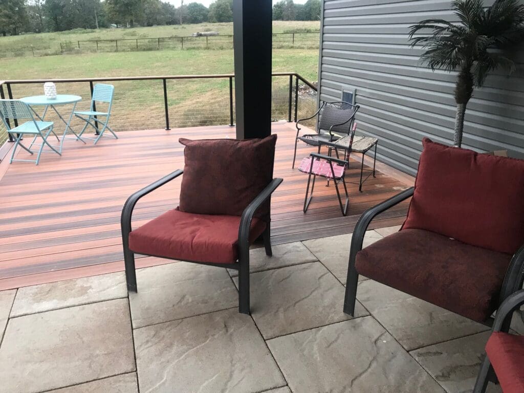 Large outdoor space with new sunburst decking, custom railing, large textured tiling, and patio chairs.